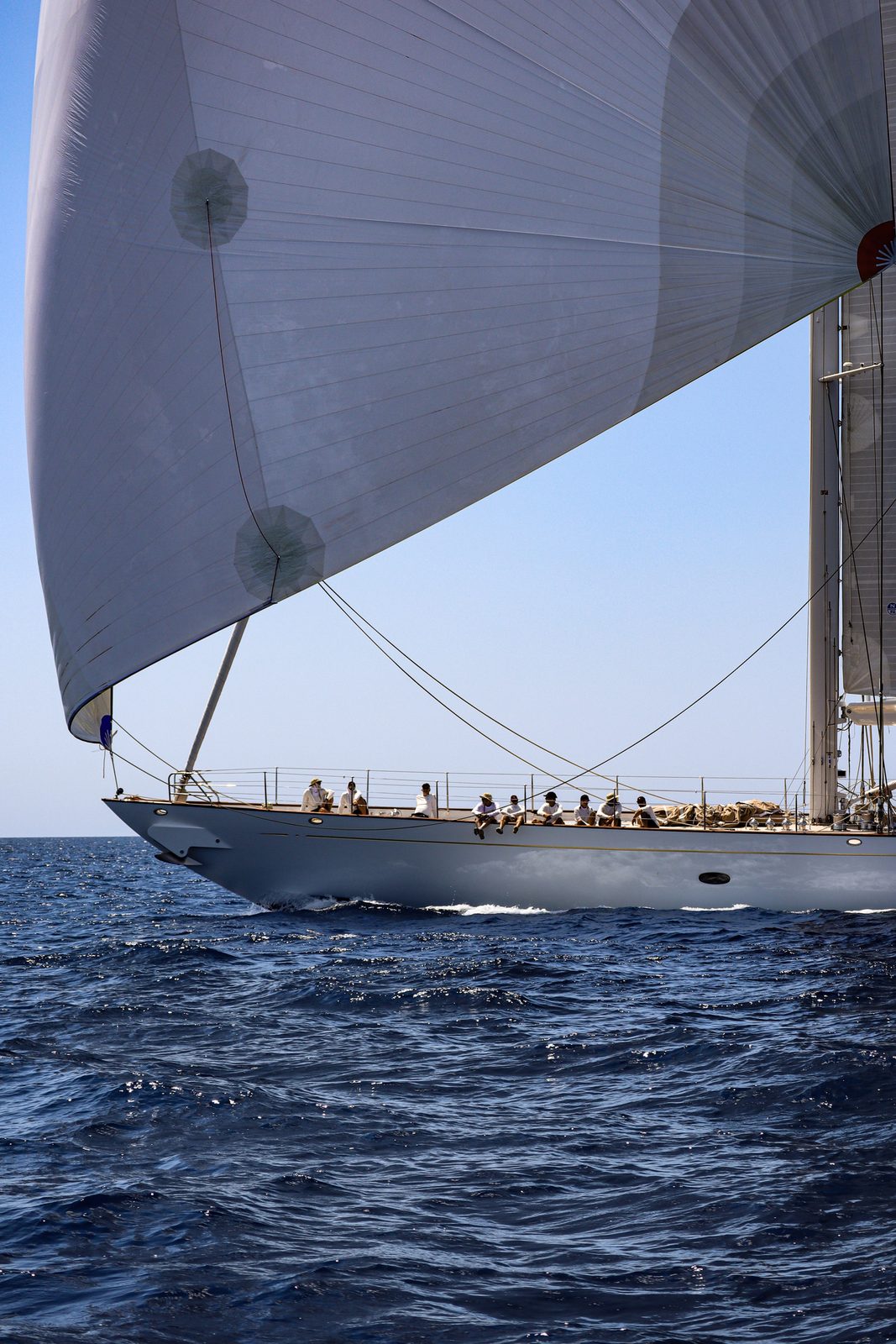 Classic sailing yacht with crew on deck cutting through deep blue sea
